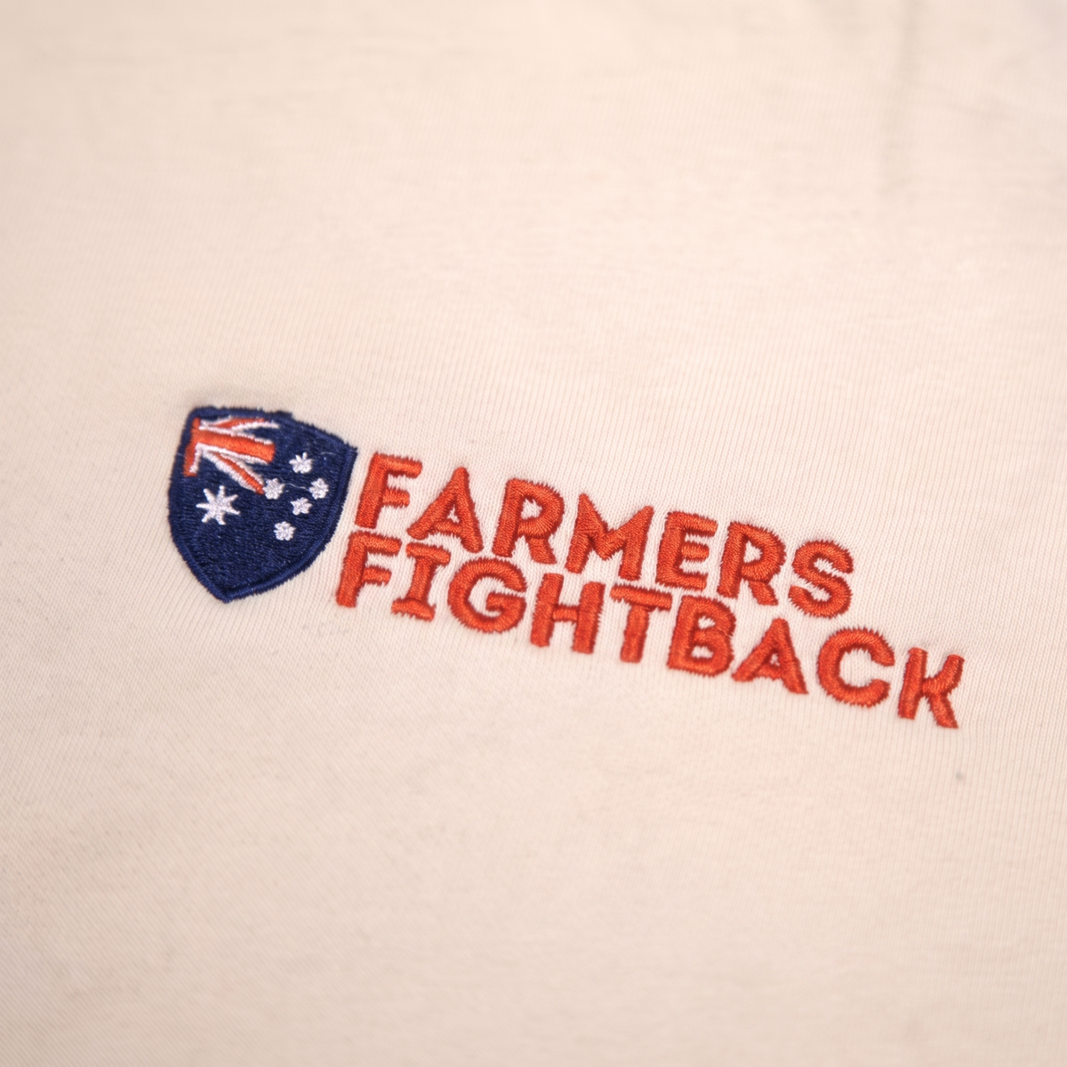 Close up of the embroidered Farmers Fightback badge on cream fabric